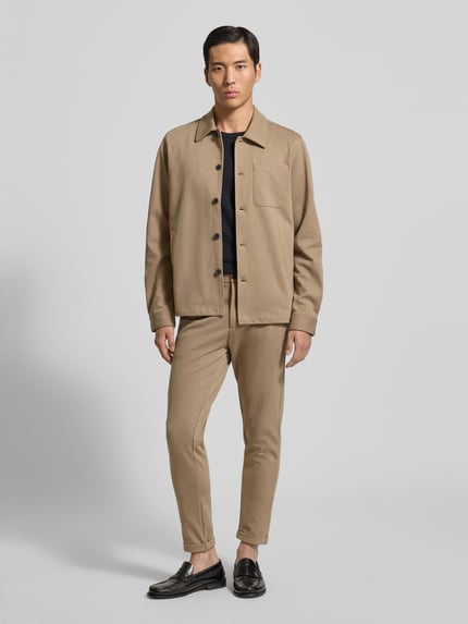 Männermodel trägt Hemdjacke mit Knopfleiste von Lindbergh in Beige, Kentkragen, Regular Fit, Brust- und Eingrifftaschen, Ganzkörperansicht von vorne.