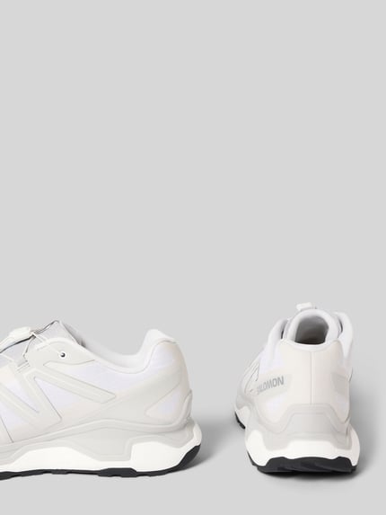 Produktfoto, Sneaker mit profilierter Sohle Modell 'XC ROAM' von Salomon, weiß-graue Farben, Logo, runde Spitze, strukturierte Textur.
