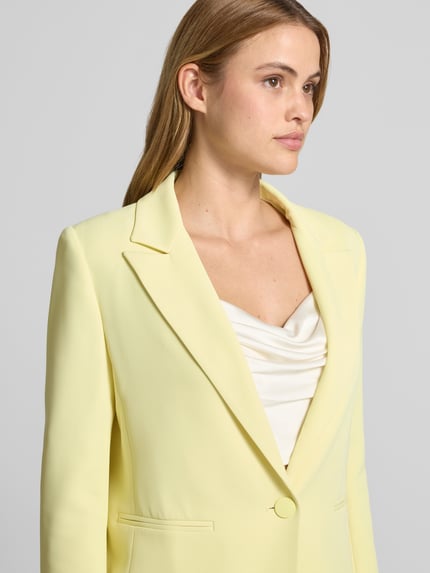 Frauenmodel trägt Blazer mit Reverskragen Modell 'REWI' von Rinascimento, hellgelb, Stretch-Materialmix, Nahaufnahme Oberkörper.