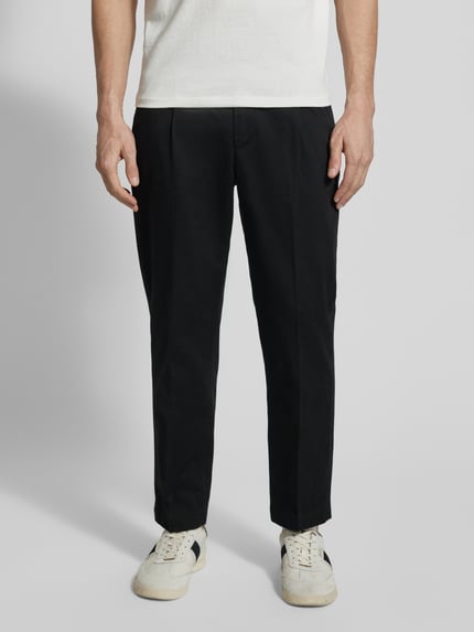 Männermodel trägt Regular Fit Chino aus katoenmix model 'TAAMIR PLEATED' van Armedangels, look: effen, logostitching, steekzakken, ganzkörperansicht von vorne.