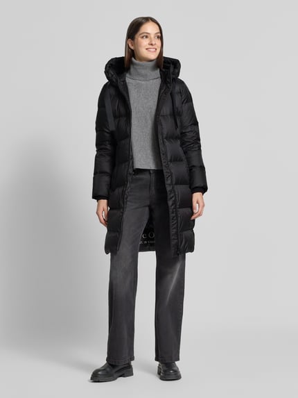 Frauenmodel trägt Regular Fit Daunenmantel mit Label-Print von Marc O'Polo in Schwarz mit glatter Textur, Ganzkörperansicht von vorne. Kontext: Damen Daunenmantel von Marc O'Polo