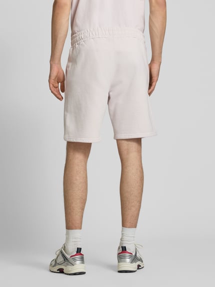 Männermodel trägt Regular Fit Shorts mit Logo-Stitching von Pegador aus Baumwoll-Mix in Hellrosa, elastischer Bund, Ganzkörperansicht Rückansicht.