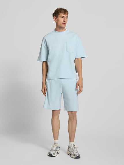 Mężczyzna nosi szorty z fakturowanym wzorem i wyhaftowanym logo 'Shorts mit Strukturmuster und Label-Stitching' od PROHIBITED, krój regular fit, bawełna, jasnoniebieski kolor, elastyczny pas, szerokość w rozmiarze M: 34 cm, długość wewnętrzna nogawki: 25 cm, całkowity widok z przodu.