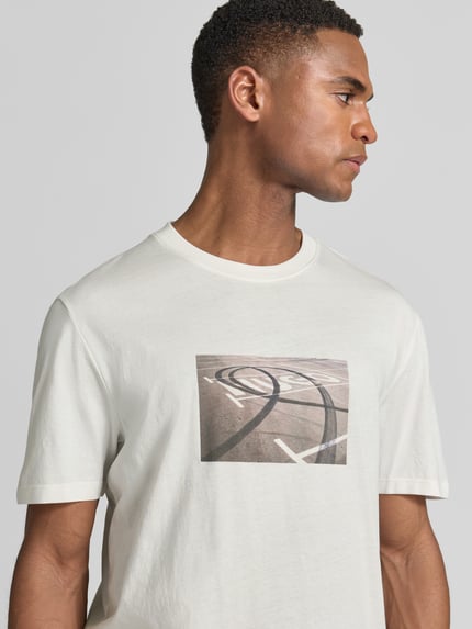 Męski model nosi Relaxed Fit T-Shirt aus reiner Baumwolle Modell 'DOSTINO' von HUGO, jednokolorowy, nadruk z logo, okrągły dekolt, krótki rękaw, dżersej, bawełna, zbliżenie na górną część ciała.