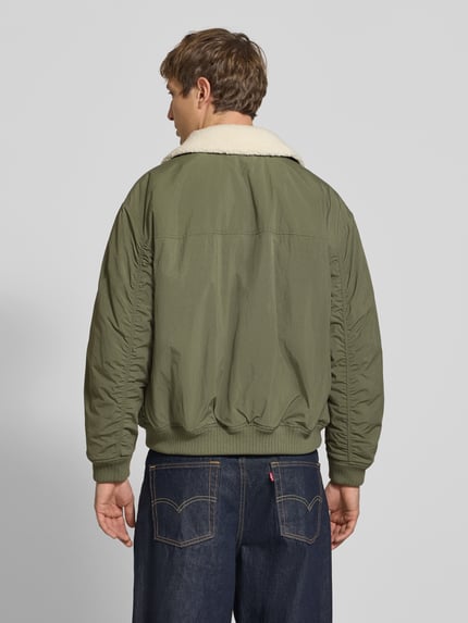 Männermodel trägt Regular Fit Bomberjacke mit abnehmbarem Teddy-Kragen von Tommy Jeans, grün, weiche Textur, Ganzkörperansicht Rückansicht, Herren Bomberjacke / Blouson.