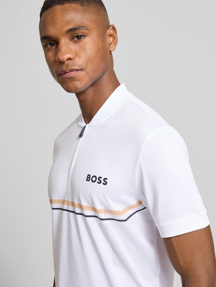 Männermodel trägt Slim Fit Poloshirt mit Logo-Print Modell 'TOC SPIN BODYMAPP 1027' von BOSS Green, Optik: Unifarben, Label-Streifen, Nahaufnahme Oberkörper.