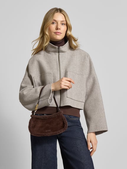 Frauenmodel trägt Handtasche mit Teddyfell Modell 'OLLIE' von Staud, braun, Hauptfach mit Reißverschluss, Label-Detail, Ganzkörperansicht von vorne.
