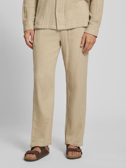Męski model nosi Straight Fit Sweatpants in Musselin-Optik von Lindbergh, spodnie dresowe z bawełny, kolor beżowy, struktura muślinu, elastyczny pas z tunelem, szerokość w rozmiarze M 41 cm, długość wewnętrzna nogawki 81 cm, ganzkörperansicht von vorne.