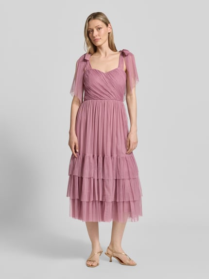 Frauenmodel trägt knielanges Cocktailkleid im Stufen-Look von LACE & BEADS aus Mesh in A-Linie mit Drapierungen, Ganzkörperansicht von vorne. Rückenlänge bei Größe S: 104 cm, Brustweite bei Größe S: 40 cm.