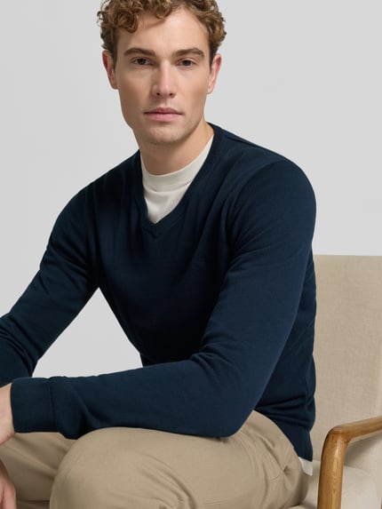 Männermodel trägt Pullover mit Logo-Stitching von S.OLIVER CASUAL in Dunkelblau, Strickstruktur, V-Ausschnitt, Nahaufnahme Oberkörper.
