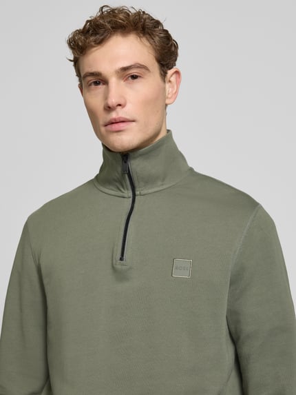 Męski model nosi Regular Fit Troyer aus reiner Baumwolle Modell 'TERRY' od BOSS Orange, zielony, jednolity, materiał sweat, długi rękaw, prosty kołnierz troyer, label patch, krótki zamek, krój regular fit, bawełna, zbliżenie górnej części torsu.