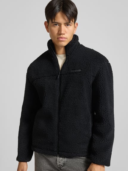 Männermodel trägt Fleecejacke mit Label-Detail und Reißverschluss von REVIEW in Schwarz, Teddyfell-Textur, Ganzkörperansicht von vorne.