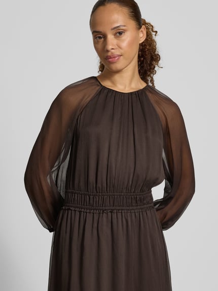 Frauenmodel trägt Maxikleid in semitransparentem Design von COMMA, tailliert, Rundhalsausschnitt, Raffungen, langärmelig, Nahaufnahme Oberkörper.