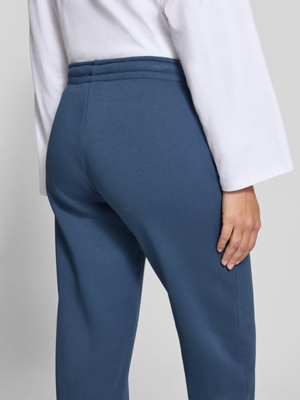 Frauenmodel trägt Sweatpants aus Baumwoll-Mix mit Tunnelzug Modell 'Iconic' von Gina Tricot in Blau, glatte Struktur, Ganzkörperansicht Rückansicht. Damen Sweatpants, Straight Fit, elastischer Bund, Innenbeinlänge bei Größe S: 76 cm.