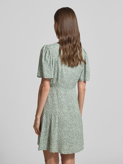 Frauenmodel trägt Leicht ausgestelltes Minikleid aus reiner Viskose Modell 'ALBA' von Vero Moda, grün mit weißen Punkten, Ganzkörperansicht Rückansicht.