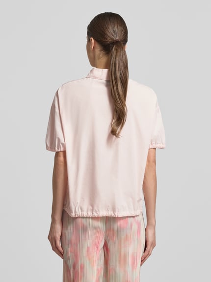 Frauenmodel trägt Regular Fit Bluse mit Polokragen von Marc Cain in zartem Rosa, Reine Baumwolle, elastische Ärmelabschlüsse, Bund mit Tunnelzug, kurzärmeliges Design, Rückenlänge 59 cm bei Größe 36, Ganzkörperansicht Rückansicht.