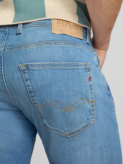 Männermodel trägt Regular Fit Jeans im Used-Look Modell 'Grover' von Replay, katoenmix met stretch, recht model, 5-pocketmodel, knoop- en ritssluiting, blauwe denim met lichte used-look, bandwijdte 43 cm, binnenbeenlengte 80 cm, detailaufnahme achterkant.