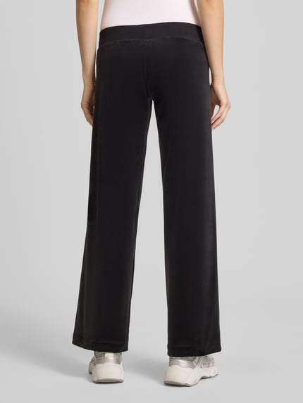 Vrouwenmodel draagt sweatpants met siersteentjes model 'GOTHIC CROWN' van Juicy Couture, materiaalmix met stretch, straight fit, elastische band, tunnelkoord, binnenbeenlengte maat S 78 cm, zwart, gladde stof, glanzend, geheel lichaam achteraanzicht.