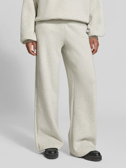 Frauenmodel trägt Sweatpants aus reiner Baumwolle von ROTATE in hellem Beige mit gerader Passform und elastischem Bund, Nahaufnahme Unterkörper.