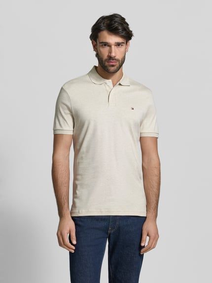 Männermodel trägt Regular Fit Poloshirt aus reiner Baumwolle Modell 'LIQUID COTTON' von Tommy Hilfiger in Melange-Optik, Logo-Stitching, Polokragen, Kurzarm, gerippte Abschlüsse, Seitenschlitze, natürliche Farbtonstruktur, Ganzkörperansicht von vorne.