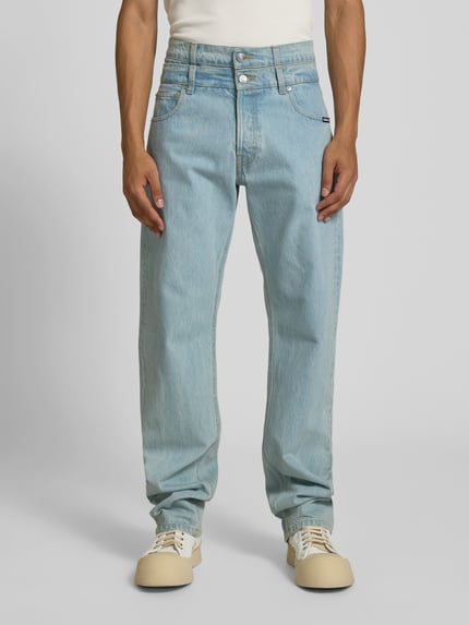 Męski model nosi Regular Fit Jeans mit Label-Detail od VETEMENTS z bawełny, 5 kieszeni, jasnoniebieski, zapięcie na guzik i zamek błyskawiczny, szerokość w rozmiarze 25: 37 cm, długość wewnętrzna nogawki: 88 cm, zdjęcie całej sylwetki z przodu.