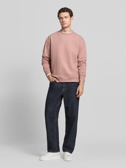 Männermodel trägt Sweatshirt mit Logo-Stitching Modell 'asher crew' von AllSaints, altrosa, unifarben, Rundhals, Rippstrick, Ganzkörperansicht von vorne.