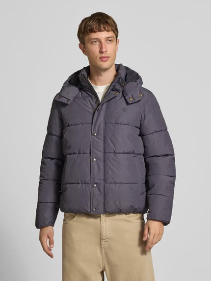 Männermodel trägt Steppjacke mit Kapuze und Reißverschluss von Superdry in Grau, sichtbare Knopfleiste, Ganzkörperansicht von vorne. Regular Fit, Stehkragen, verdeckter Reißverschluss, Rückenlänge 71 cm, Schulterbreite 50 cm, Brustweite 56 cm, Ärmellänge 83 cm.