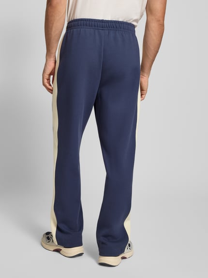 Männermodel trägt Sweatpants mit Längsnähten und Label-Print von KARL KANI, Blau mit cremefarbenen Einsätzen, Material-Mix, Ganzkörperansicht Rückansicht.