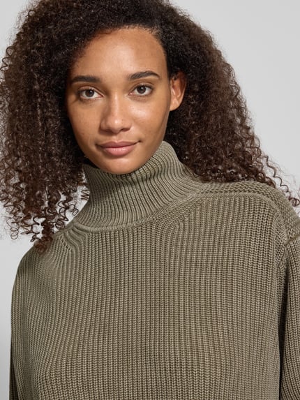 Frauenmodel trägt Oversized Turtleneck-Pullover aus reiner Baumwolle von G-Star RAW in Olivgrün mit grober Strickstruktur, Nahaufnahme Oberkörper.