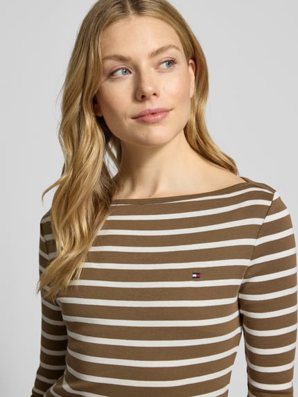 Frauenmodel trägt Slim Fit T-Shirt aus reiner Baumwolle von Tommy Hilfiger, Optik: Allover-Muster, gestreift, Logo-Stitching, U-Boot-Ausschnitt, 3/4-Arm, Feinstrick, Nahaufnahme Oberkörper.