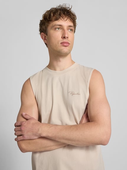 Männermodel trägt Tanktop mit Label-Stitching und Rundhalsausschnitt von Pegador in Beige, reine Baumwolle, Relaxed Fit, Nahaufnahme Oberkörper.