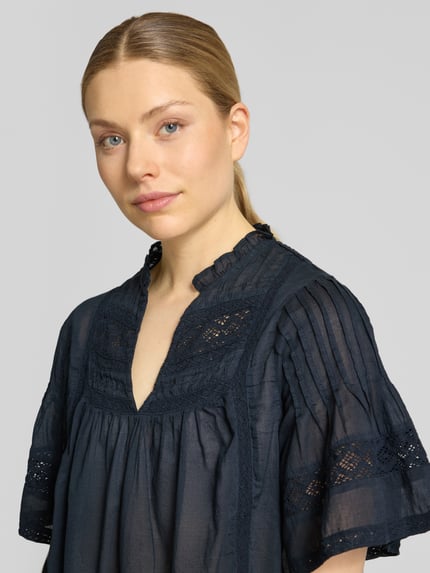 Frauenmodel trägt Blusenshirt mit V-Ausschnitt Modell 'Siama' von Neo Noir in Dunkelblau mit Stitchings, Regular-Fit, Nahaufnahme Oberkörper. Rückenlänge bei Größe 36: 56 cm, Ärmellänge bei Größe 36: 28 cm.