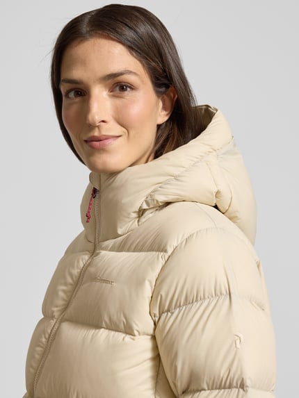 Frauenmodel trägt Steppjacke mit Label-Stitching Modell 'FROST DOWN' von PEAK PERFORMANCE in Beige mit Kapuze, Reißverschluss, Nahaufnahme Oberkörper. Regular Fit, Rückenlänge 64 cm, Schulterbreite 41 cm, Brustweite 56 cm, Ärmellänge 64 cm, Damen.