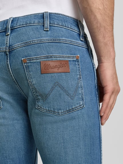 Mężczyznamodel nosi jeansy im Used-Look model 'Greensboro' von Wrangler, mieszanka bawełny i elastanu, krój slim fit, wpuszczane kieszenie, szerokość w rozmiarze 32/32: 42 cm, długość wewnętrzna nogawki w rozmiarze 32/32: 77 cm, detalowanie tylnych kieszeni, niebieski denim, tekstura lekko znoszona, detalaufnahme tylnej kieszeni.