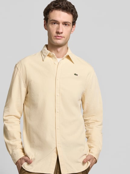 Männermodel trägt Regular Fit Cordhemd mit Logo-Applikation von LACOSTE in einfarbigem Beige mit Struktur, Nahaufnahme Oberkörper.
