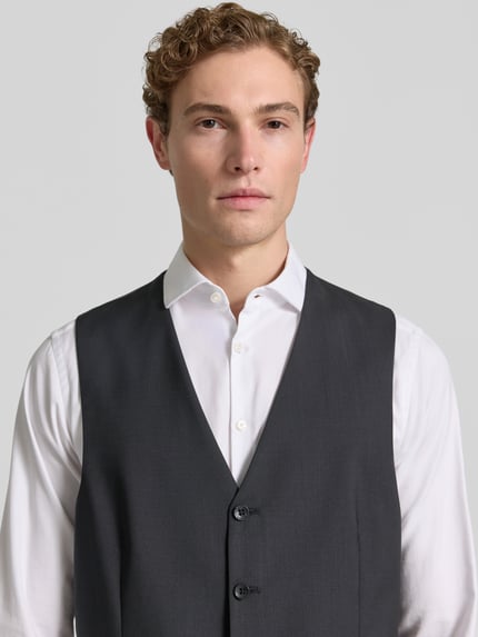 Männermodel trägt Weste mit V-Ausschnitt und Paspeltaschen Modell 'Tobias' von Carl Gross, Reine Schurwolle, Slim-Fit, Knopfleiste, Nahaufnahme Oberkörper.