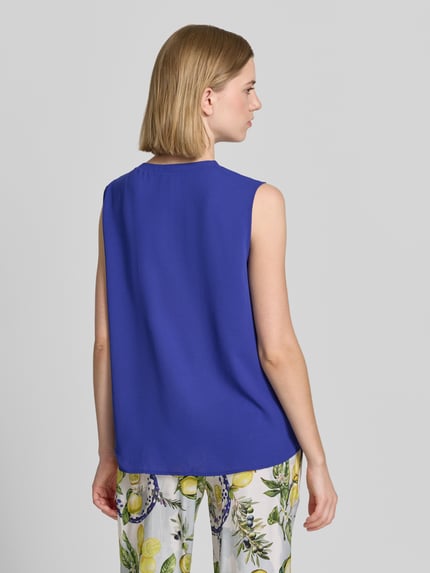 Frauenmodel trägt Regular Fit Bluse mit Zierschleife von Marc Cain in Blau, ärmelloses Design, Rückenlänge 62 cm, Ganzkörperansicht Rückansicht.