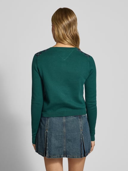 Frauenmodel trägt Regular Fit Strickjacke aus reiner Baumwolle von Tommy Jeans in Dunkelgrün, kombiniert mit Jeansrock; Ganzkörperansicht Rückansicht, Damen Strickjacke von Tommy Jeans.