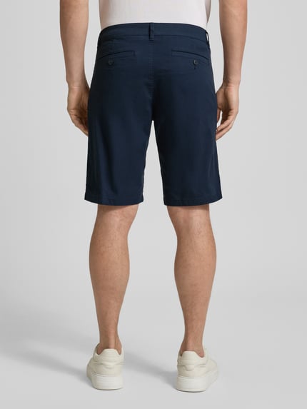 Männermodel trägt Regular Fit Bermudas aus Baumwoll-Mix Modell 'PHOENIX' von s.Oliver RED LABEL in Dunkelblau, Ganzkörperansicht Rückansicht. Unifarbene, cropped Herren-Bermudas mit Gürtelschlaufen, 5-Pocket-Design und glatter Twill-Oberfläche.