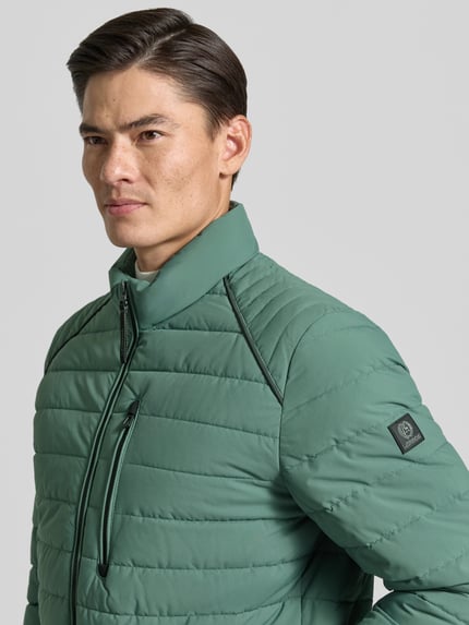 Männermodel trägt Steppjacke mit Stehkragen und Reißverschlusstaschen von LERROS in grün, Regular Fit, Nahaufnahme Oberkörper.