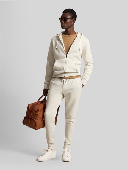 Męski model nosi Regular Fit Sweatjacke aus Baumwoll-Mix von Polo Ralph Lauren w kolorze kremowym, gładka tekstura, całopostaciowy widok z przodu.