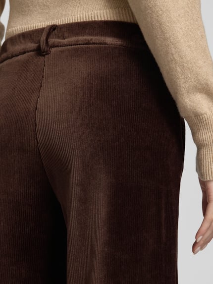 Frauenmodel trägt Regular Fit Cordhose mit Bundfalten Modell 'MAINE' von BRAX in Dunkelbraun, Cordstruktur, Gürtelschlaufen, Nahaufnahme Rückansicht.