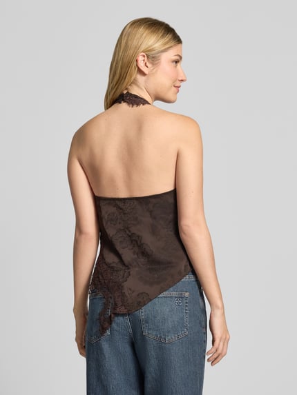 Frauenmodel trägt Blusentop mit Spitzenbesatz von VERO MODA in Unifarbe mit floraler Spitze, Neckholder, Cut Out, asymmetrischer Saum, Ganzkörperansicht Rückansicht.