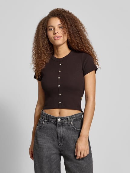 Kobiece modelka nosi Cropped T-Shirt mit Knopfleiste Modell 'Heritage' od G-Star Raw, czarny, bawełniano-elastanowy, faktura prążkowana, okrągły dekolt, widoczne detale, widok całej sylwetki z przodu.