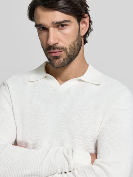Męski model nosi Regular Fit Koszulka polo w imitacji dzianiny Model 'Riley' od Jack & Jones Premium z bawełny, krój regular fit, kołnierzyk polo, z długim rękawem, długość tyłu w rozmiarze M: 56 cm, kremowy, faktura dzianiny, zbliżenie na górną część ciała.