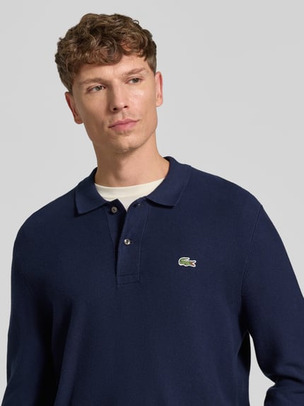 Męski model nosi Regular Fit Poloshirt aus reiner Baumwolle od Lacoste, granatowy kolor, gładka faktura, zbliżenie na górną część ciała.