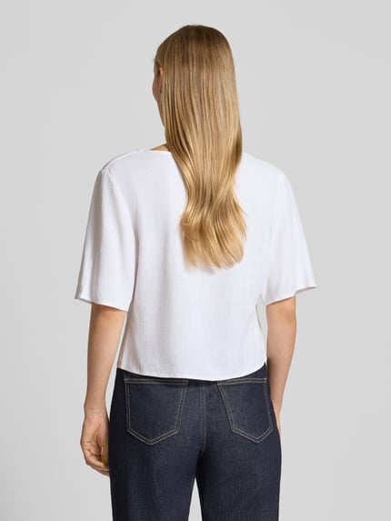 Vrouwenmodel draagt 'Hemdbluse aus Viskose-Mix mit Leinen-Anteil' van Apricot, rechte fit, V-hals, knoopsluiting, half lange mouw, wit, gladde textuur, ruglengte 46 cm, mouwlengte 28 cm, jeans, Ganzkörperansicht achteraan.
