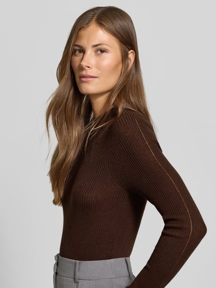 Frauenmodel trägt Strickpullover mit Woll-Anteil von MYON, Ripp-Optik, Lochmuster vorn, eng anliegend, Nahaufnahme Oberkörper.