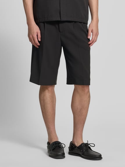 Mężczyzna nosi Straight Fit Shorts mit Viskose-Anteil von Lindbergh, czarne, matowa tkanina, kieszenie, Szerokość w rozmiarze M: 44 cm, długość nogawki: 30 cm, Ganzkörperansicht von vorne.