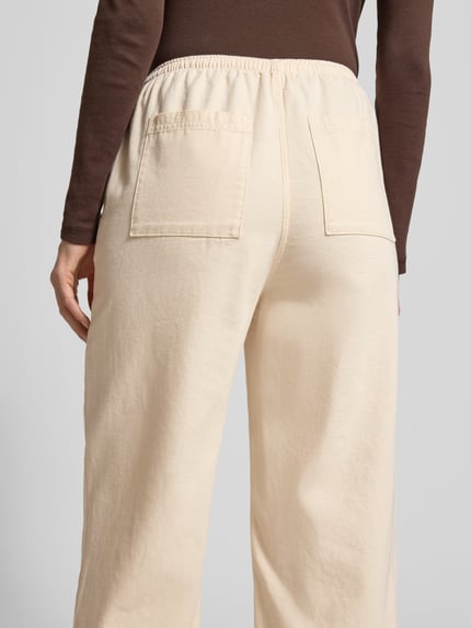 Frauenmodel trägt Wide Fit Stoffhose mit elastischem Bund Modell 'Lycaz' von American Vintage in Beige, reine Baumwolle, Ganzkörperansicht Rückansicht.